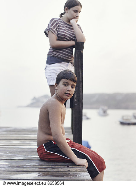 Two young people  teenagers  boy and girl  on a dock overlooking moored boats on the coastline.