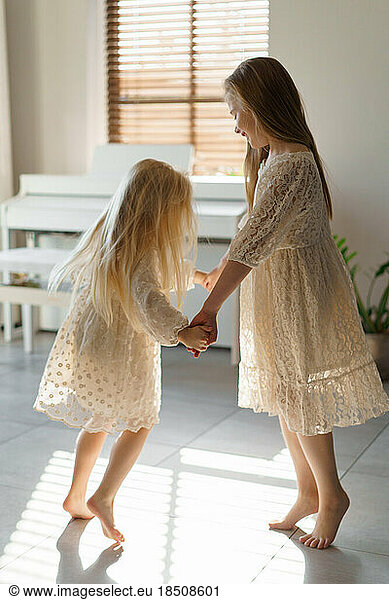 Two young sisters dancing indoors.