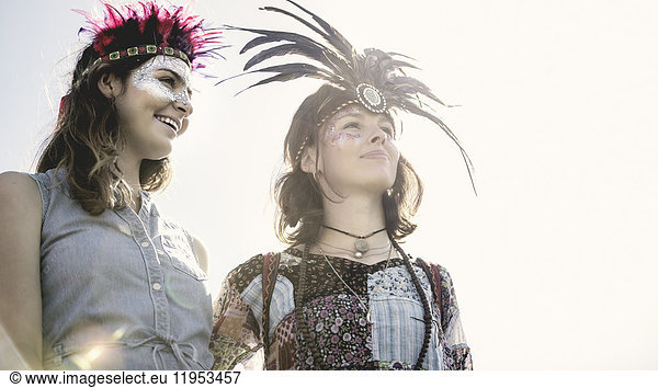 Two young women at a summer music festival faces painted  wearing feather headdresses.