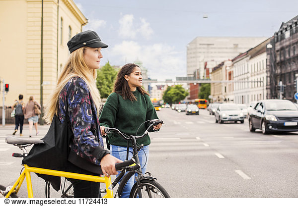 Two young women pushing bikes in town