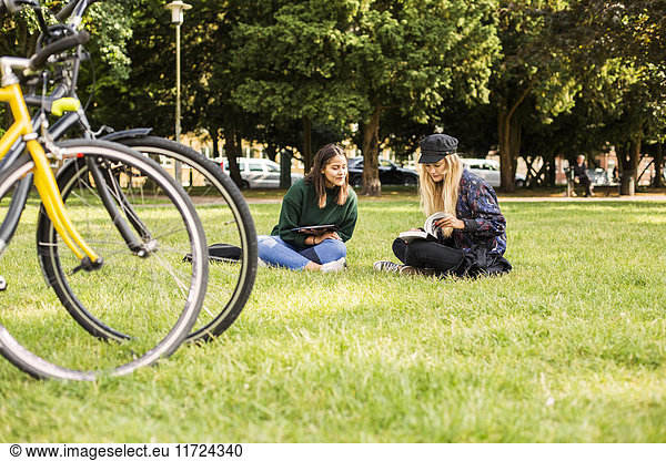 Two young women sitting in park  bicycle in foreground