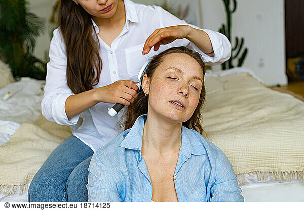 Two young women sitting together at home  one brushing another's hair