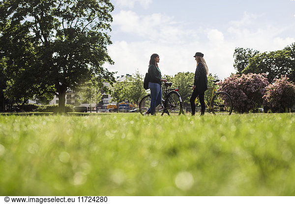 Two young women standing with bicycles in park