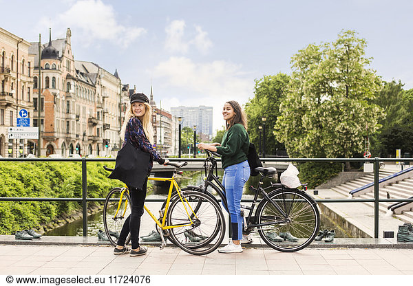 Two young women standing with bicycles on footbridge