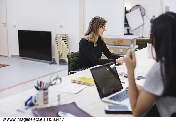 Two young women working at desk in creative office