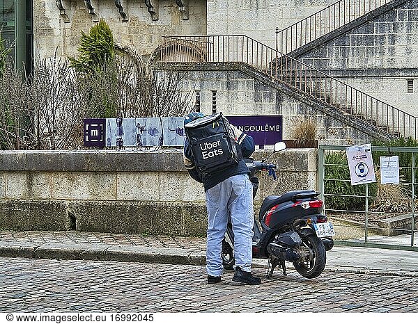 Uber Eats delivery driver and motor scooter outside Angouleme Cathedral  Angouleme  Charente Department  Nouvelle-Aquitaine  France.