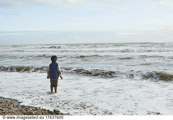 UK  Devon  Rear view of boy in oversized sweater looking at sea waves