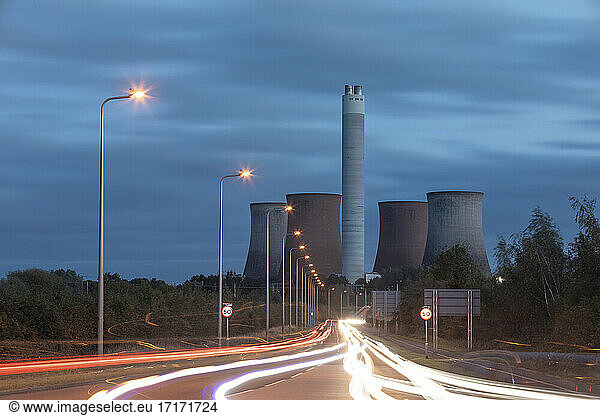 UK  England  Rugeley  Vehicle light trails stretching along illuminated road at dusk with cooling towers in background