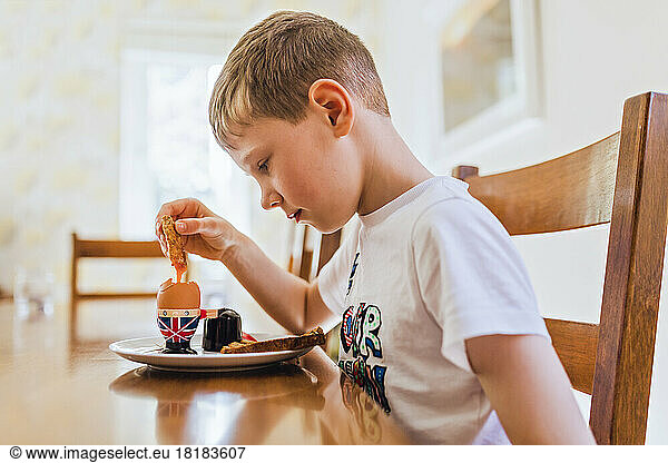 UK  sad boy sitting at breakfast table eating boiled egg
