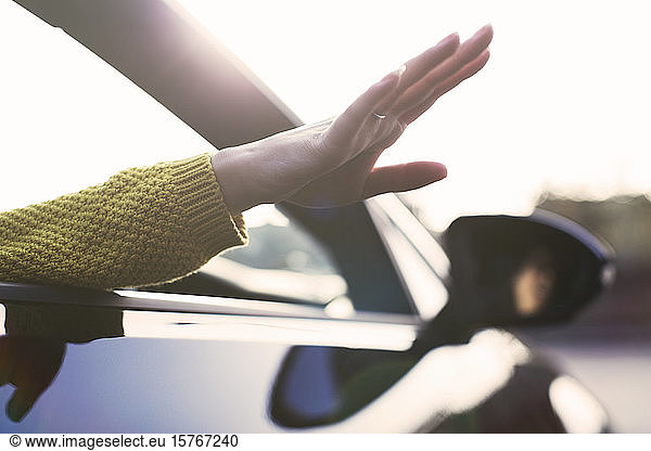 Unbekümmerte Frau streckt die Hand aus dem Autofenster