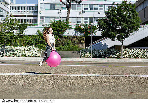 Unbekümmerte Geschäftsfrau  die an einem sonnigen Tag auf einem Ball hüpft