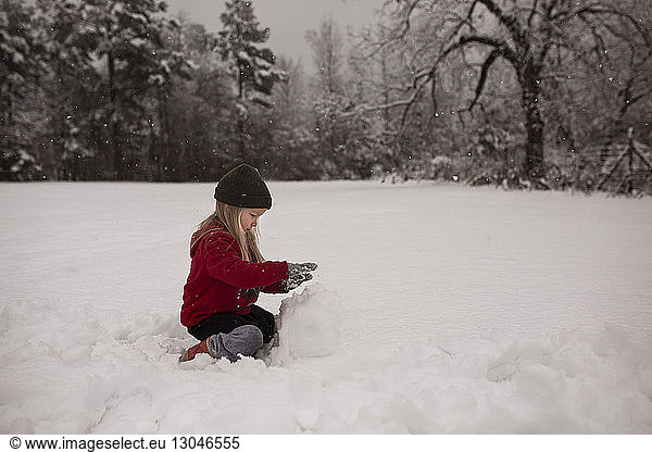 Unbekümmertes Mädchen macht Schneemann auf verschneitem Feld