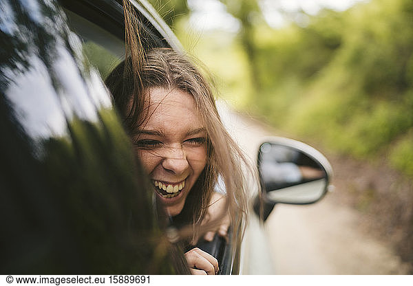 Unbeschwerte junge Frau lehnt sich aus dem Autofenster
