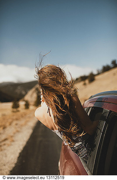 Unbeschwerte junge Frau mit zerzaustem Haar  die sich aus dem Autofenster lehnt