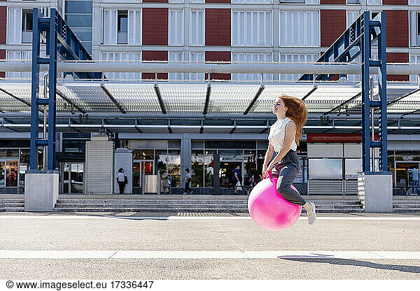 Unbeschwerte weibliche Freiberuflerin springt mit Hüpfball bei Gebäude während sonnigen Tag