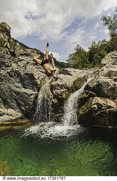 Unbeschwerter Mann ohne Hemd macht Purzelbaum am Wasserfall