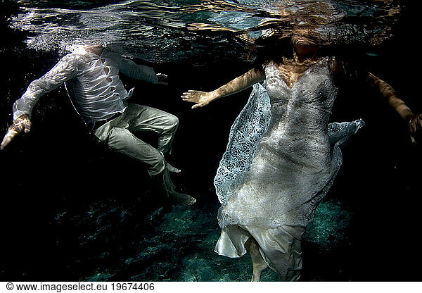 Underwater image of a man and woman swimming in their wedding clothes in a cenote.