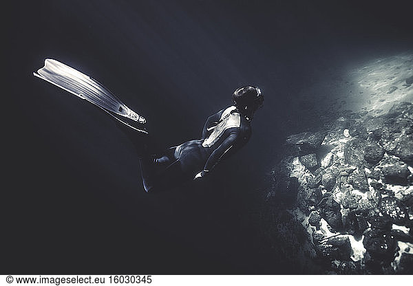 Underwater view of diver wearing wet suit and flippers  diving near rocks.