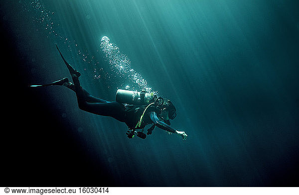Underwater view of diver wearing wetsuit  diving goggles and oxygen cylinder  air bubbles rising.