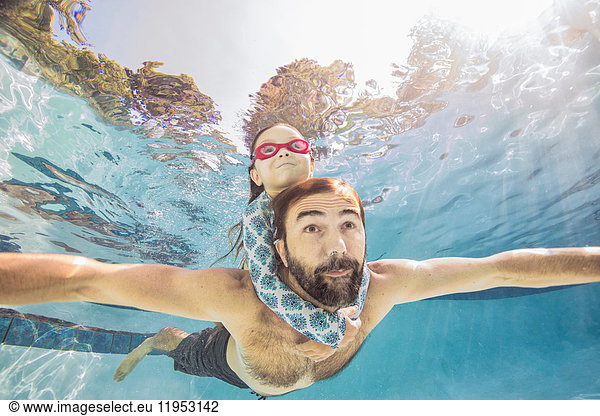 Underwater view of mature man swimming with daughter on piggy back