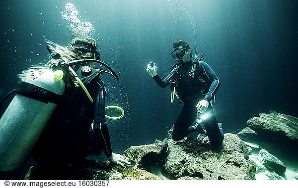 Underwater view of two divers wearing wetsuits  diving goggles and oxygen cylinders.