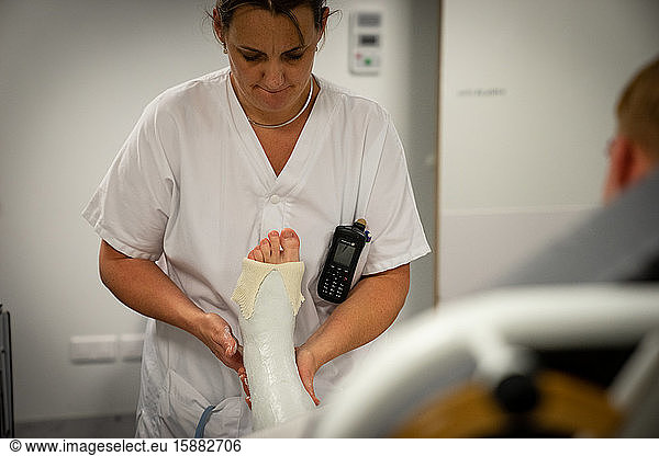 Une jeune femme présentant un hématome important à la cheville et une fracture est plâtrée. La cadre de santé et l'infirmier positionnent le pied en position de flexion avant de le plâtrer.