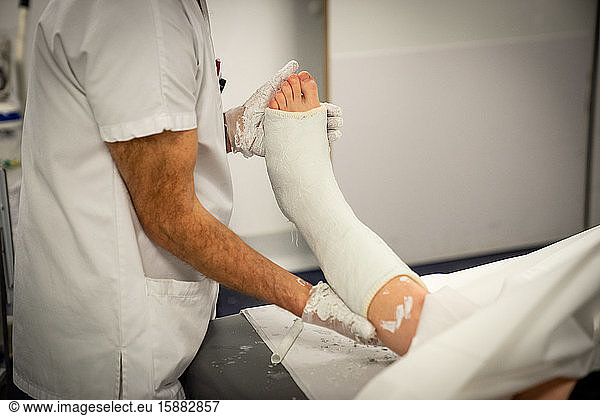 Une jeune femme présentant un hématome important à la cheville et une fracture est plâtrée. La cadre de santé et l'infirmier positionnent le pied en position de flexion avant de le plâtrer.