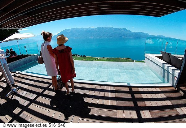UNESCO World Heritage site - Lavaux vineyards on terraces  two woman admiring panoramic view from restaurant's terrace in Chexbres  Geneva Lake  French Alps on the other side of lake  Lac Leman  Swiss Romandy  Romandie Suisse  canton Vaud  Wallis canton  VD  Switzerland  Europe
