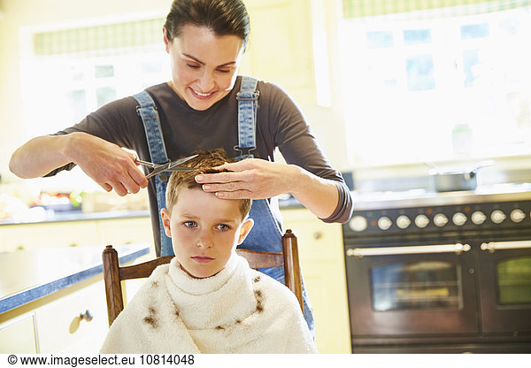 Unglücklicher Junge bekommt Haarschnitt von Mutter in der Küche