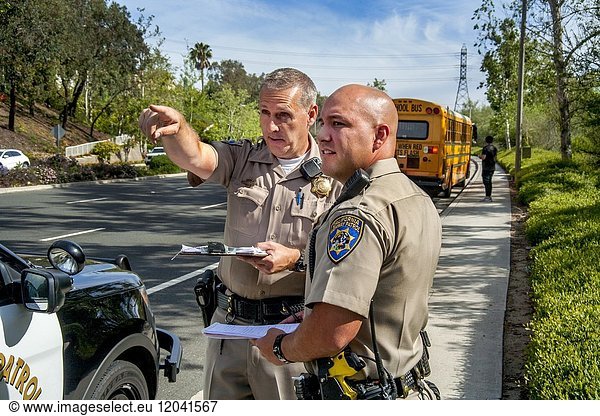 Uniformed Hispanic and Caucasian policemen observe road conditions leading to a school bus accident in Laguna Hills  CA. Note bus and driver in background.