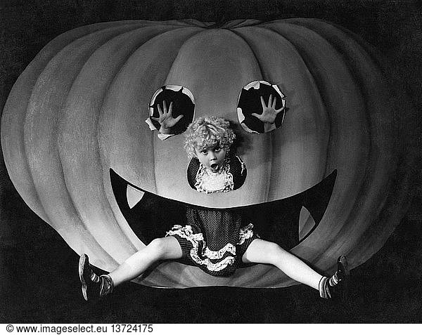 United States: c. 1927 A young girl in the mouth of a cut out pumpkin on Halloween.