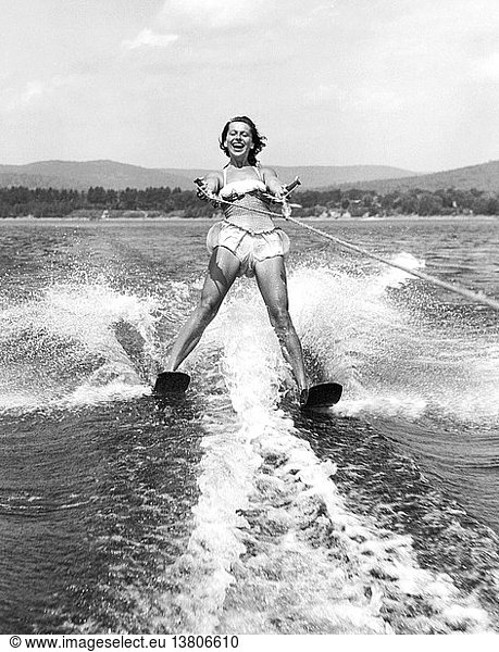 United States: c. 1955 A young woman with a big smile on her face as she water skis close behind the boat.