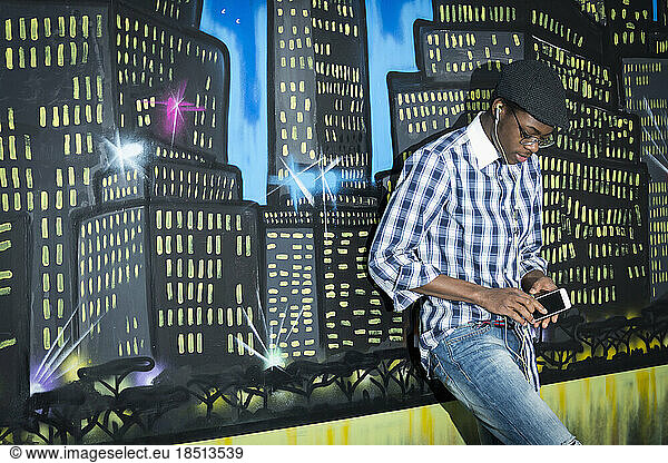 University student listening to music on mobile phone in front of night skyline graffiti wall School  Bavaria  Germany