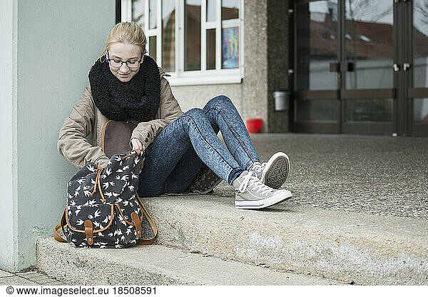 University student sitting on steps and looking for something in bag School  Bavaria  Germany