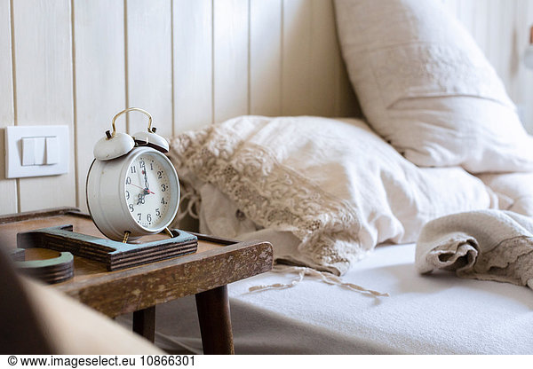 Unmade bed  alarm clock on bedside table