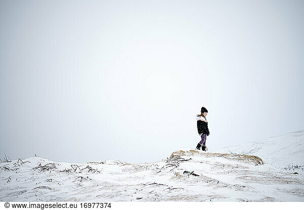 Unrecognizable kid in warm clothes walking on snowy mountain slope