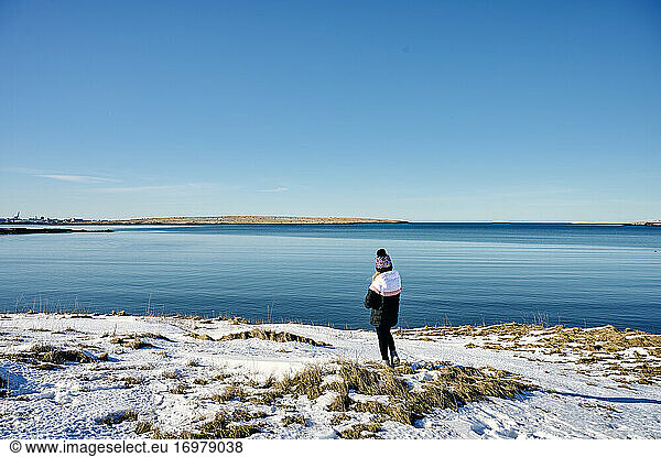 Unrecognizable lady standing on snowy seashore against cloudless blue sky