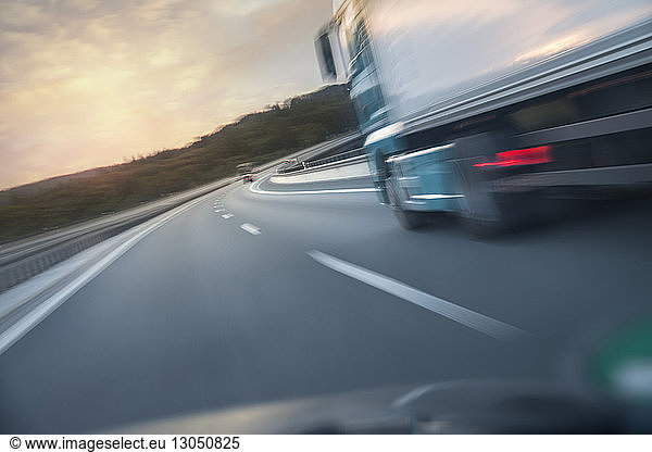 Unscharfe Bewegung eines Lastwagens  der sich bei Sonnenuntergang durch die Windschutzscheibe eines Autos auf der Straße bewegt
