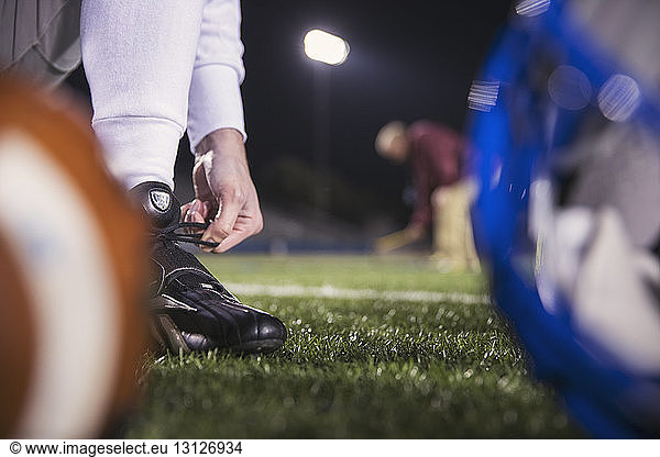 Unterer Teil eines American-Football-Spielers beim Schnürsenkelbinden auf dem Spielfeld mit dem Trainer im Hintergrund