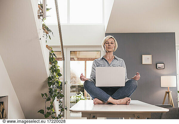 Unternehmerin mit Laptop im Lotussitz auf dem Tisch zu Hause