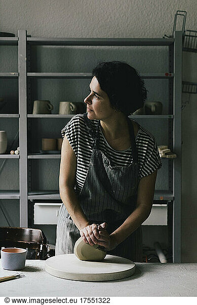 Unternehmerin schaut weg  während sie in einer Keramikwerkstatt Ton knetet