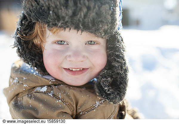 Up close of cute toddler in winter clothes and hat smiling in the snow