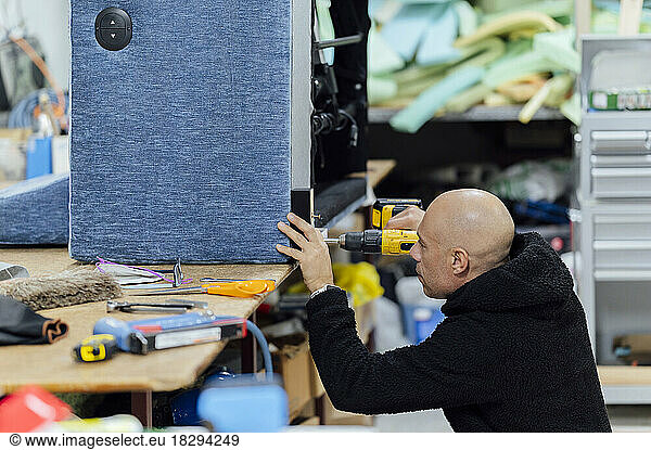 Upholsterer working with drill machine at workshop