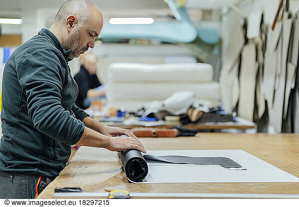 Upholstery worker rolling fabric by table in workshop