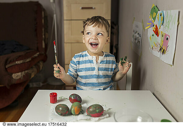 Upper body of blonde boy holding paintbrush and painting easter