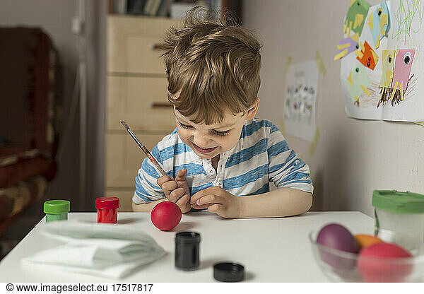 Upper body of boy looking at red easter egg