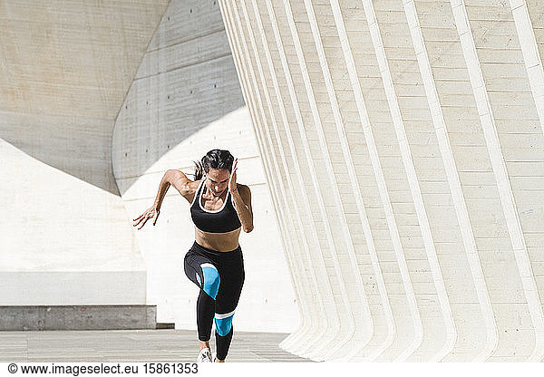 Upper body of female athlete in sportswear running fast on concrete