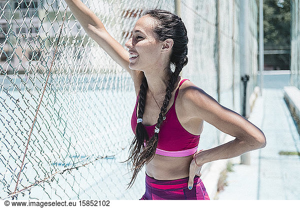 Upper body of smiley female athlete leaning on fence while resting
