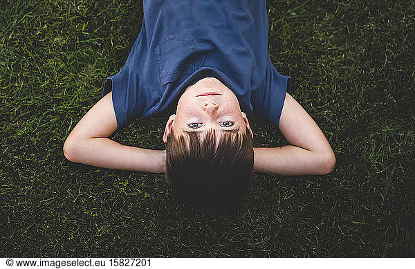 Upside down image of boy laying on grass with arms behind head.