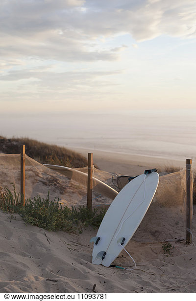 Upside down surfboard leaning against fence during sunset